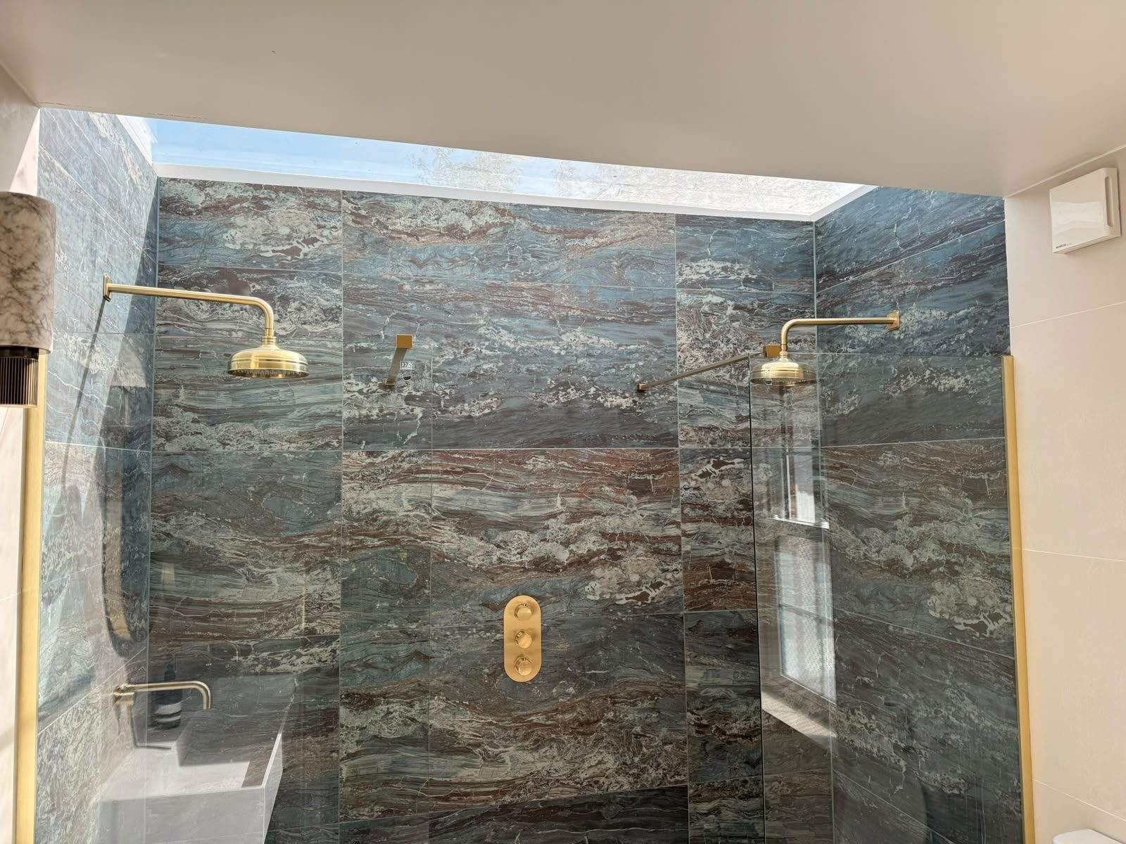 Completed walk-in shower with twin brushed-gold shower heads and marble-effect tiling, installed by JY Plumbing & Heating