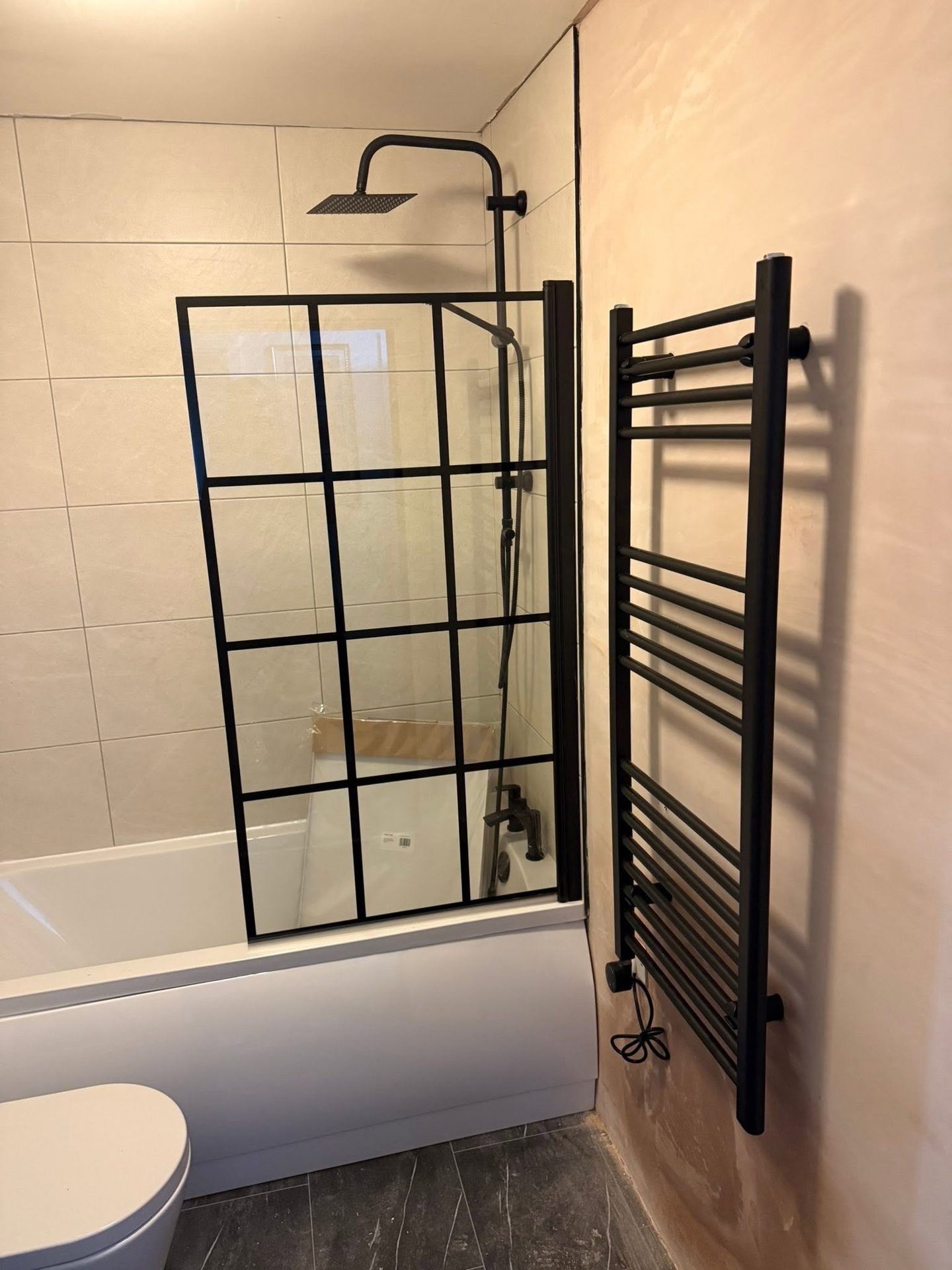 Black grid-style shower screen over a bath with a matching black towel radiator in a finished bathroom installation