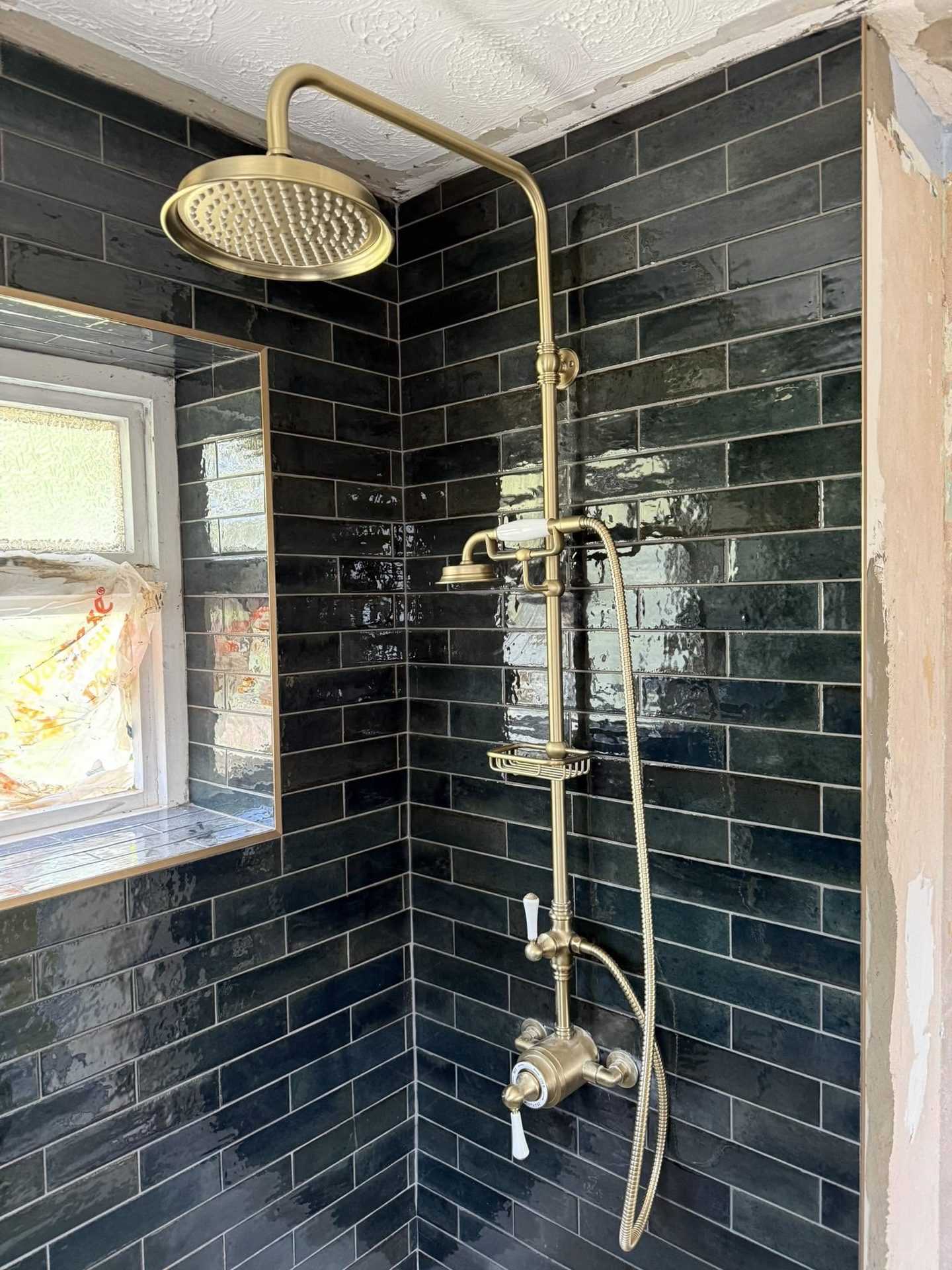 Traditional brass shower head and mixer valve installed against dark green metro tiles in a refurbished bathroom