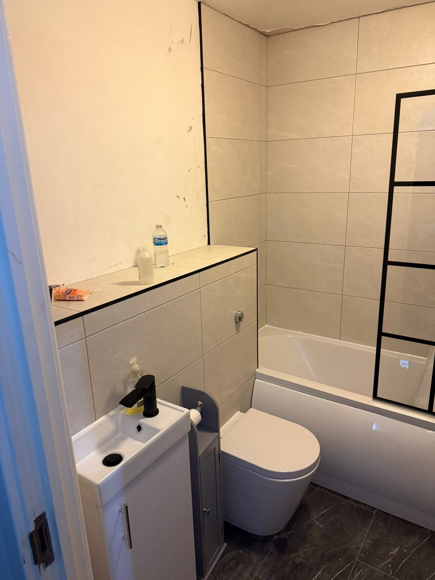 The same High Wycombe bathroom after renovation by JY Plumbing & Heating, with a new bath, black-framed screen, wall-hung basin and fresh tiling