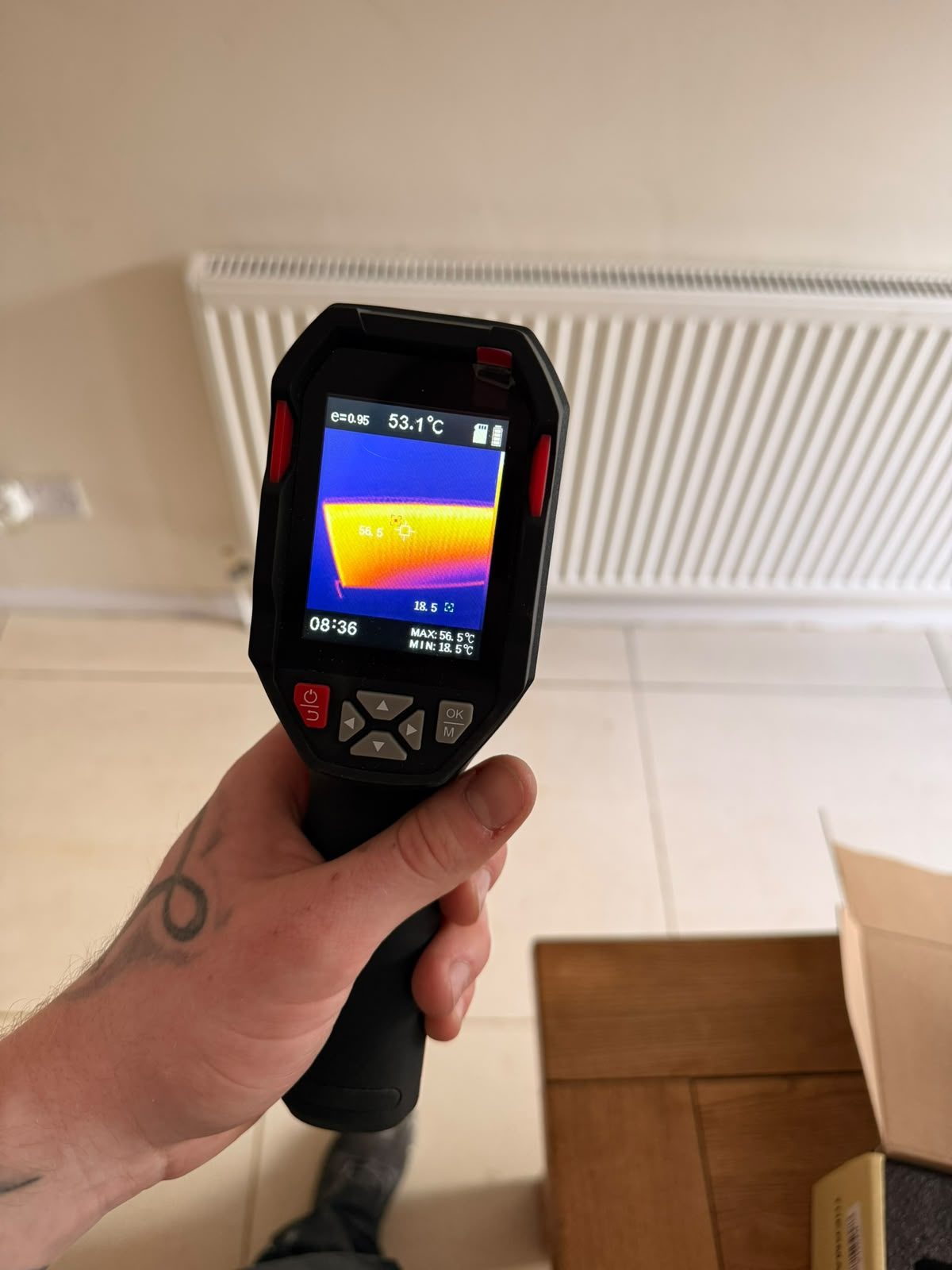 Engineer using a thermal imaging camera to survey a radiator and pipework while tracing a leak